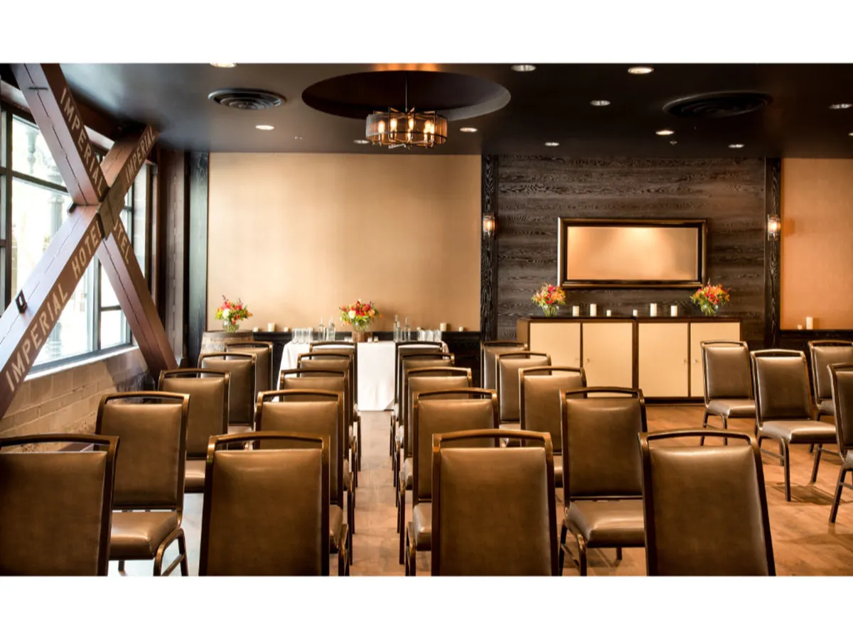 A well-appointed meeting space featuring rows of chairs arranged for a seminar or workshop, accented by elegant floral arrangements on the table and a stylish lighting fixture above. The atmosphere is formal yet welcoming, inviting productive business gatherings and meaningful discussions.