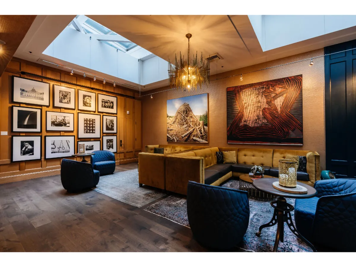 This image showcases a seating area with artwork on the walls and a statement chandelier overhead, setting a creative and welcoming tone. A cozy seating arrangement invites guests to relax and appreciate the curated art collection that nods to the hotel’s artistic heritage.