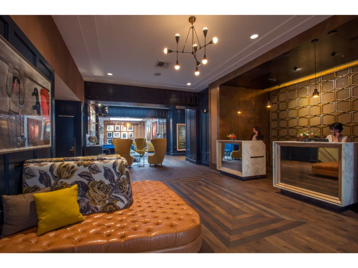 A chic and contemporary hotel lobby featuring a tufted leather sofa, a geometric reception desk, and carefully curated artwork on the walls. The stylish seating arrangement is designed for both comfort and socializing, with open spaces that invite guests to linger, relax, and strike up conversations.