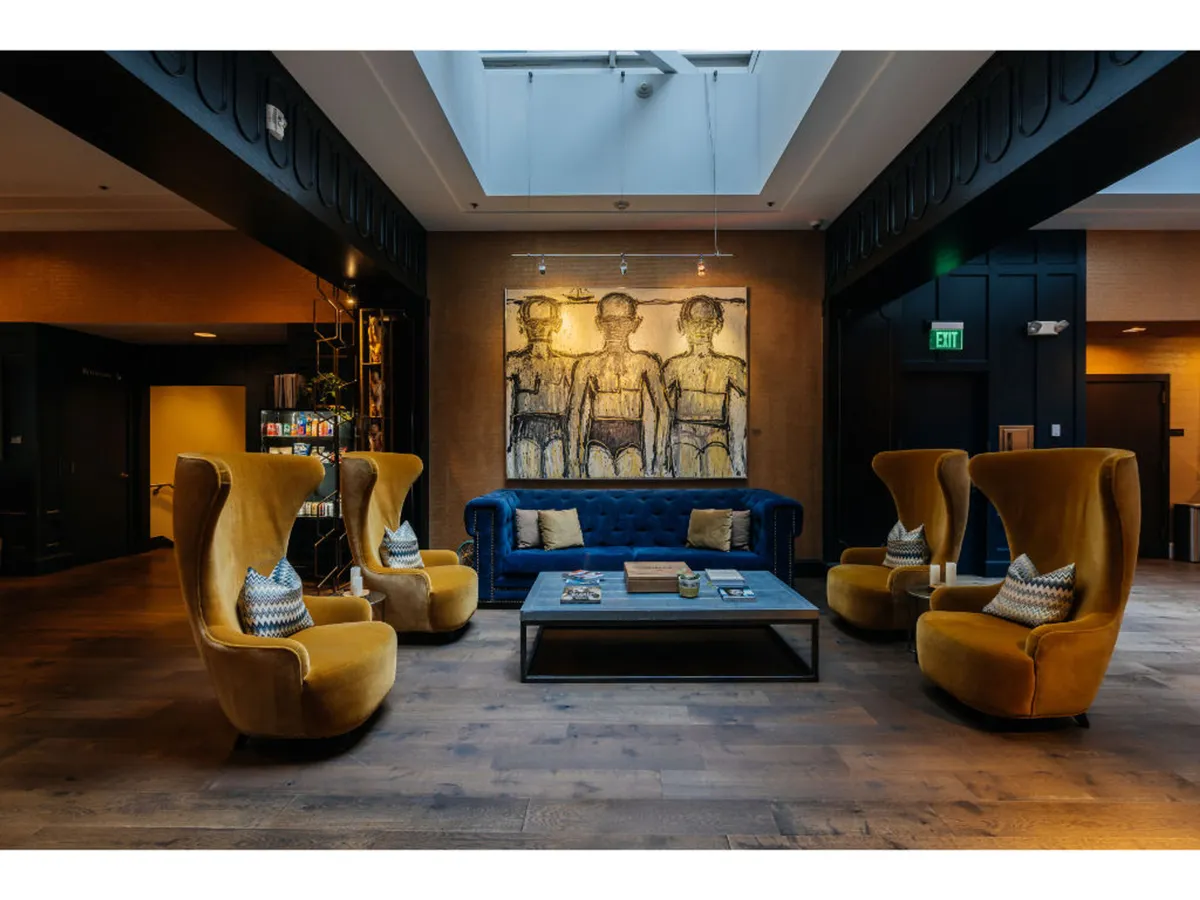 A stylish lounge setting featuring a contemporary blue sofa, cheerful yellow armchairs, vibrant artwork, and a coffee table, all arranged to invite conversation and relaxation. The space exudes an artistic, modern vibe ideal for socializing among friends.