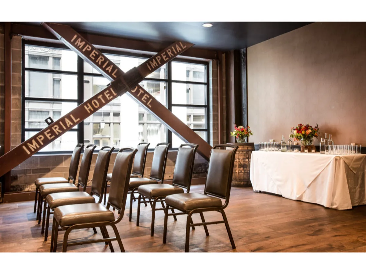 A decorative beam reading 'IMPERIAL HOTEL' is visible above an intimate arrangement of chairs and a table set with a floral arrangement and glasses. The space feels historic yet welcoming, with a layout that encourages gathering and relaxation.