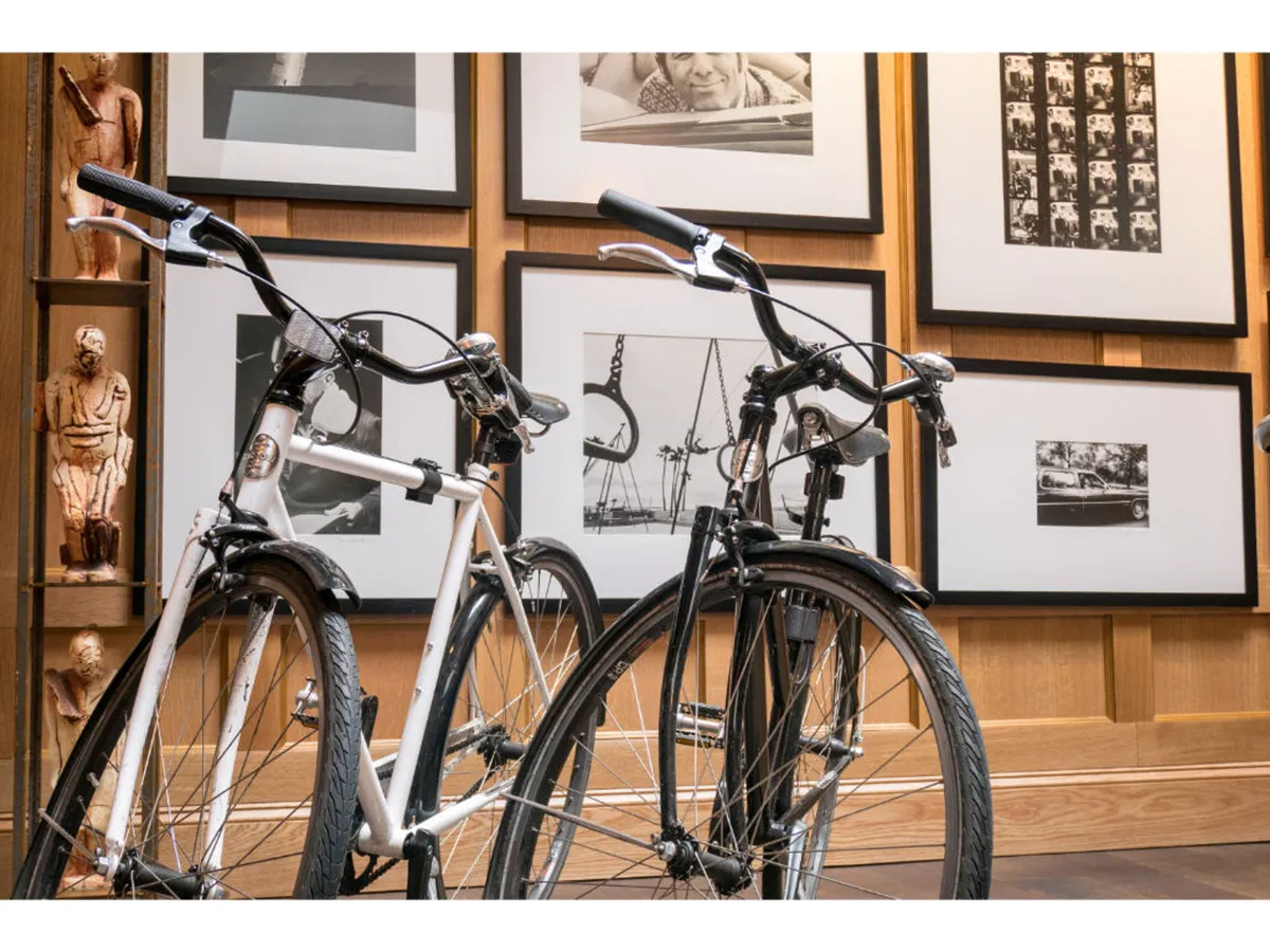 A dynamic interior scene featuring two bicycles and a striking collection of framed black and white photographs, along with a wooden sculpture. The space feels energized and community-oriented, perfect for guests to engage with local art and one another.