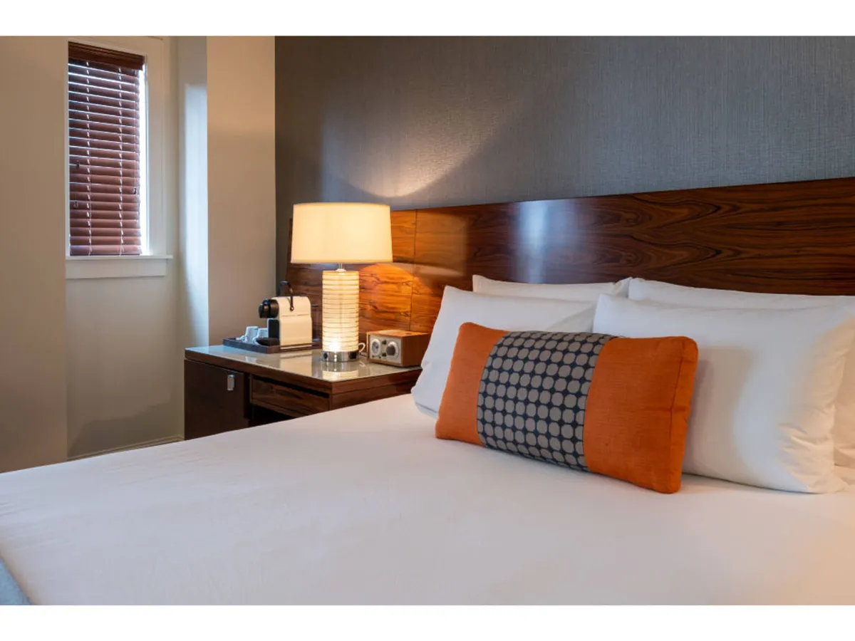 A serene bedroom scene featuring a cozy bed with a decorative pillow, a softly lit bedside lamp, and a wooden headboard, exuding relaxation and comfort.