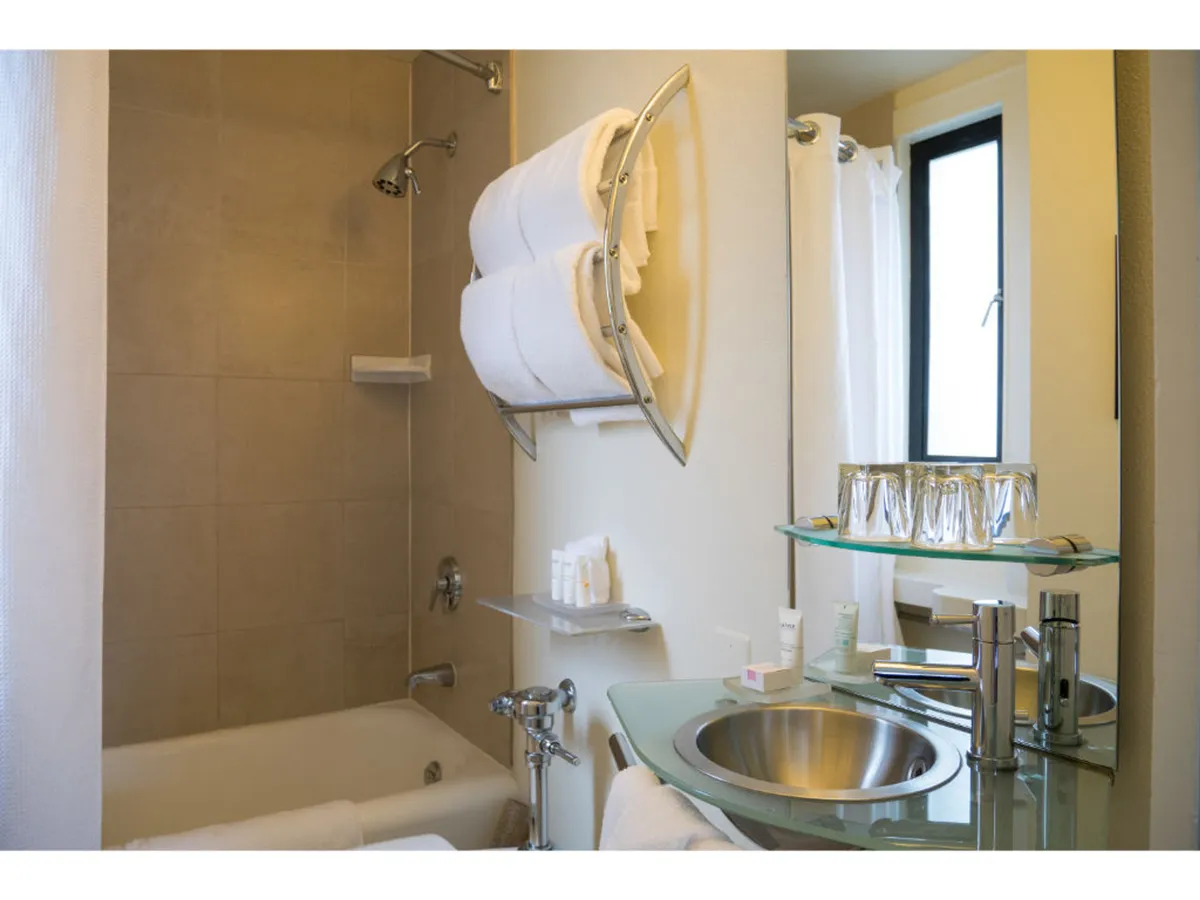 A bright, modern bathroom with a bathtub, sink, fresh towels, and a window letting in natural light. The mood is peaceful and rejuvenating.