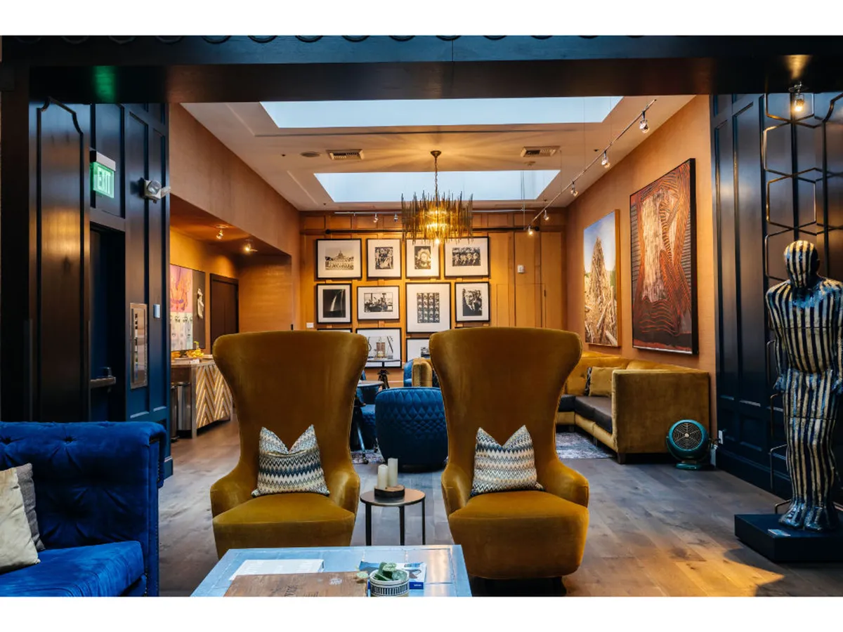 A welcoming lounge area with two large yellow armchairs, a blue sofa, modern chandelier, and eclectic artwork, set against an inviting backdrop perfect for unwinding or sharing drinks with friends.